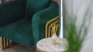 Un sofá verde con detalles dorados, una mesita redonda con superficie blanca y una planta verde.