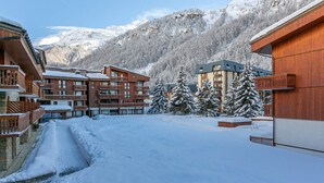 Un patio cubierto de nieve con edificios de madera, incluyendo un hotel con balcones y un paisaje montañoso de fondo.