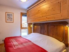 A bedroom with a wooden headboard, a red patterned throw blanket, and a framed picture on the wall.