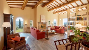 A spacious living room with wooden beams, red sofas, a fireplace, and a bookshelf.