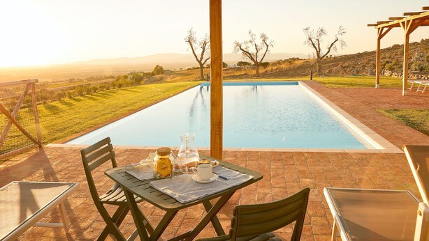 A poolside area with a table set for breakfast, overlooking a pool and a scenic landscape.