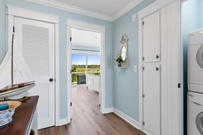 Una habitación con piso de madera, una puerta y una pared blancos, un reloj y vista a un balcón.