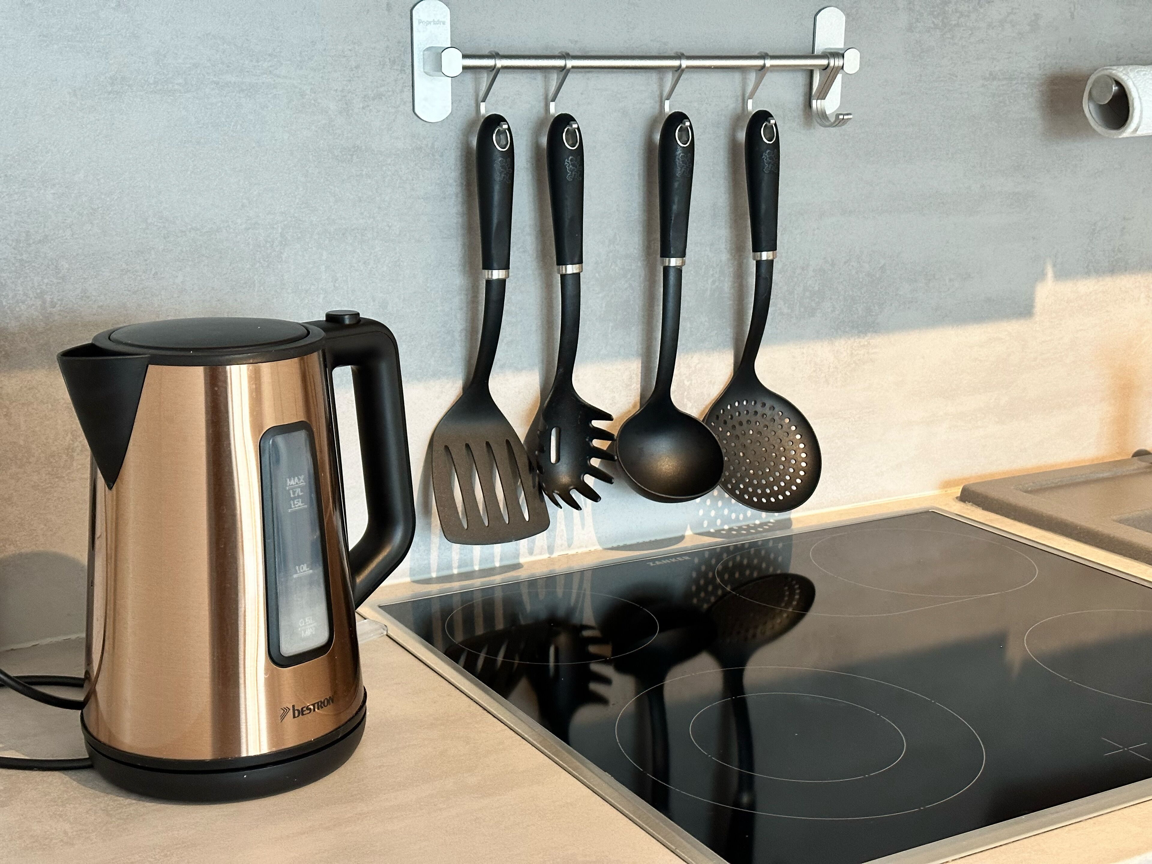 Uma cozinha com uma chaleira de aço inoxidável, uma espátula preta e uma concha penduradas em um suporte.
