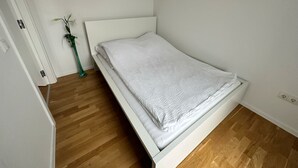 A single-bed room with a wooden floor, white walls, and a white headboard. - Modernes Apartment I Parkplatz I Terrasse I Sehr Beliebt bei Wanderer (Blumberg)