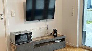 A modern living room with a flat-screen TV mounted on the wall, a built-in microwave, and a coffee maker on a wooden console table. - Modernes Apartment I Parkplatz I Terrasse I Sehr Beliebt bei Wanderer (Blumberg)