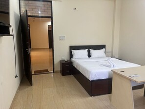Ein Hotelzimmer mit einem Bett, Nachttischen, einem Schreibtisch und einer Tür, die zu einem Flur führt.