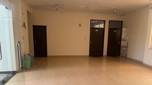 Un pasillo amplio con suelo de baldosas, dos puertas con indicaciones y un separador de vidrio a la izquierda.