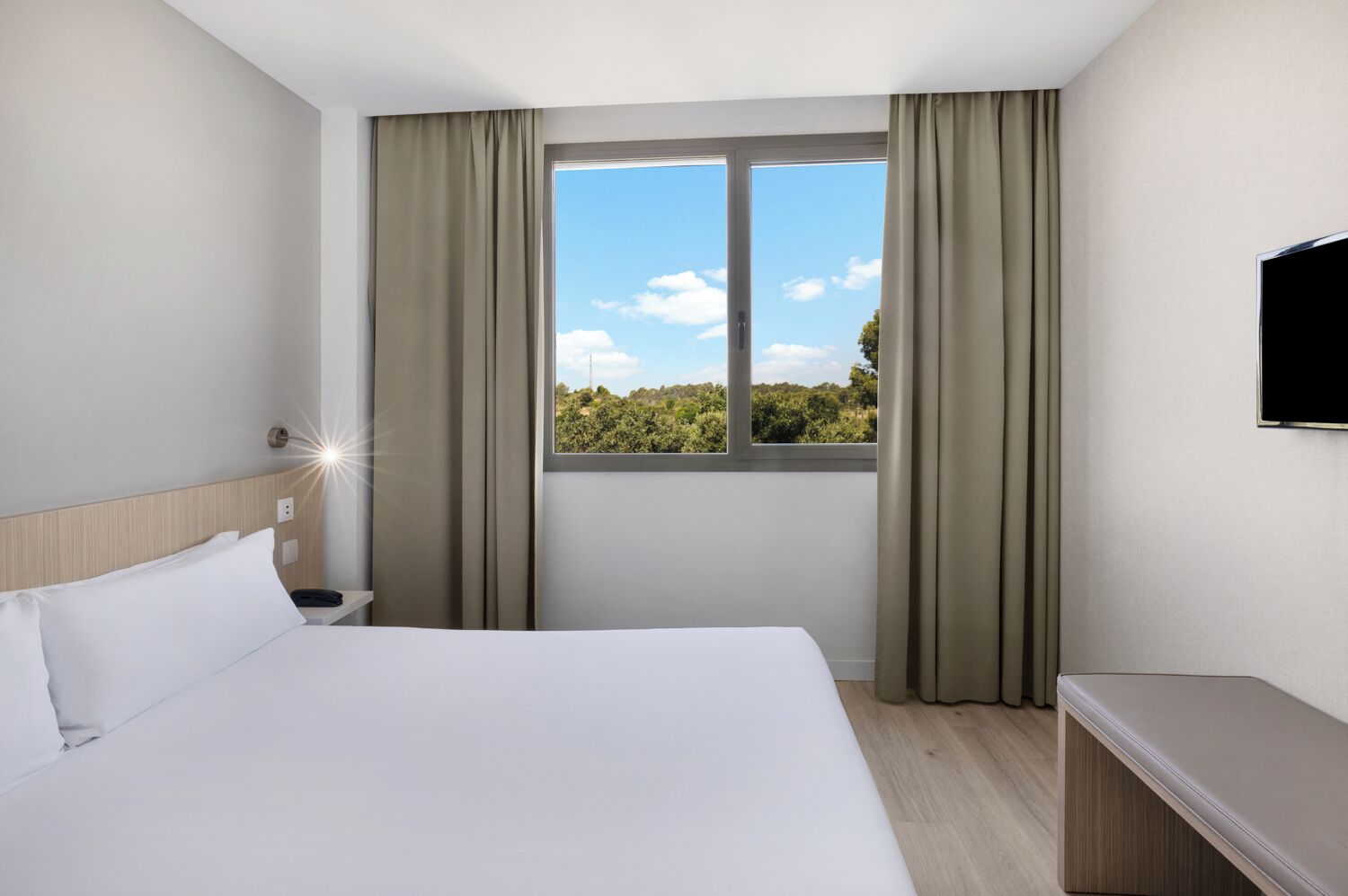 Habitación de hotel con cama, escritorio, televisor y ventana con cortinas.