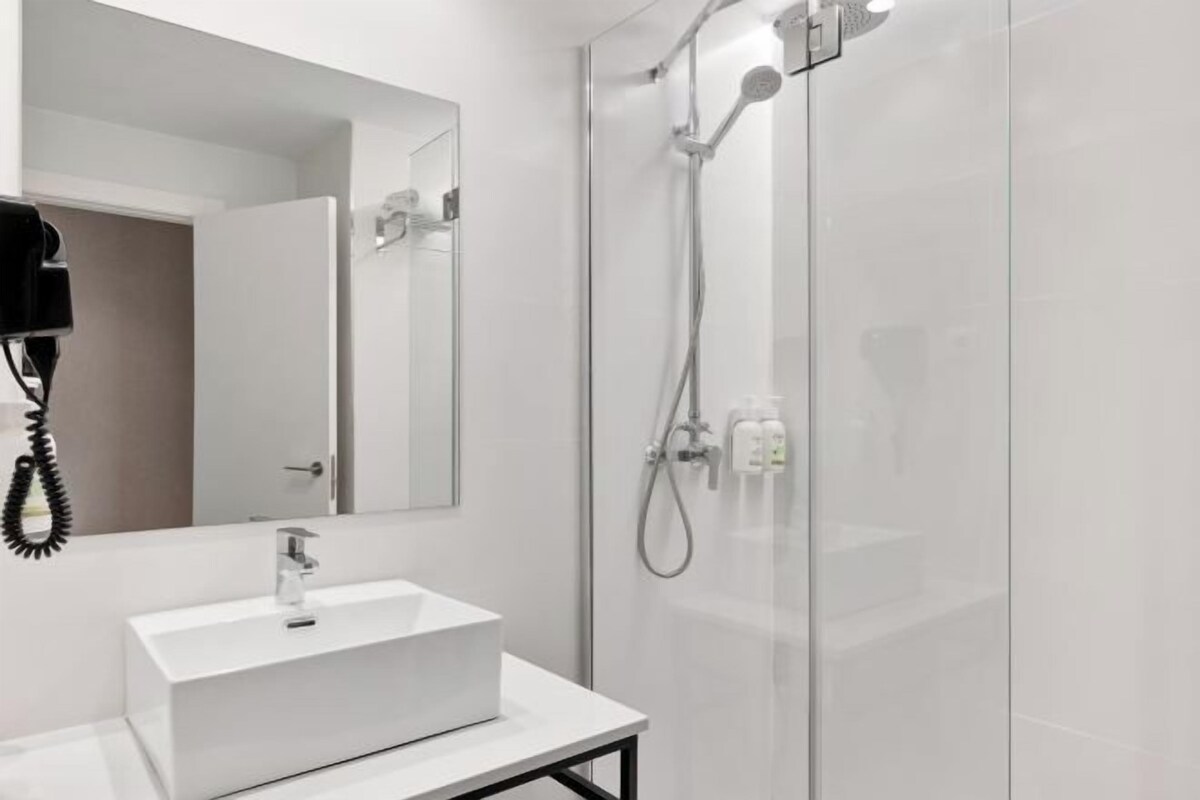 Un baño moderno con un lavamanos blanco, un espejo y zona de ducha con mampara de vidrio.