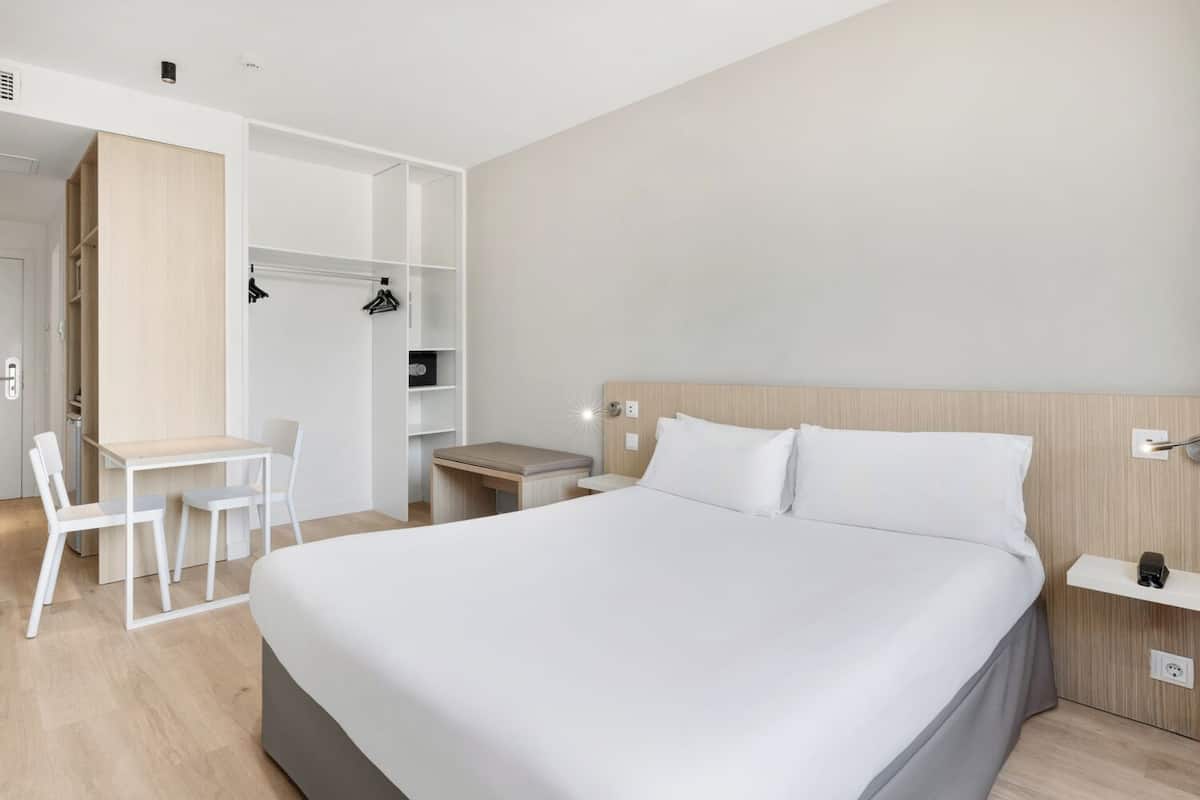 Una habitación de hotel con cama, escritorio, sillas y armario.