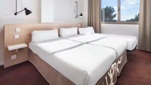 Habitación de hotel con una cama grande, dos mesitas de noche, una lámpara de pared, una ventana con cortinas y vistas a árboles.