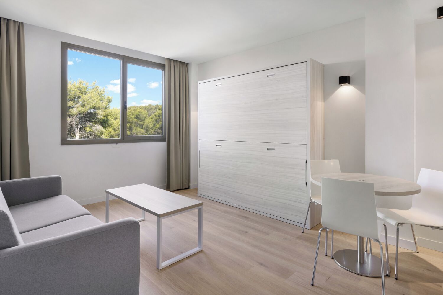 Una habitación moderna y minimalista con sofá, una mesita, un armario blanco y un comedor con mesa y sillas.