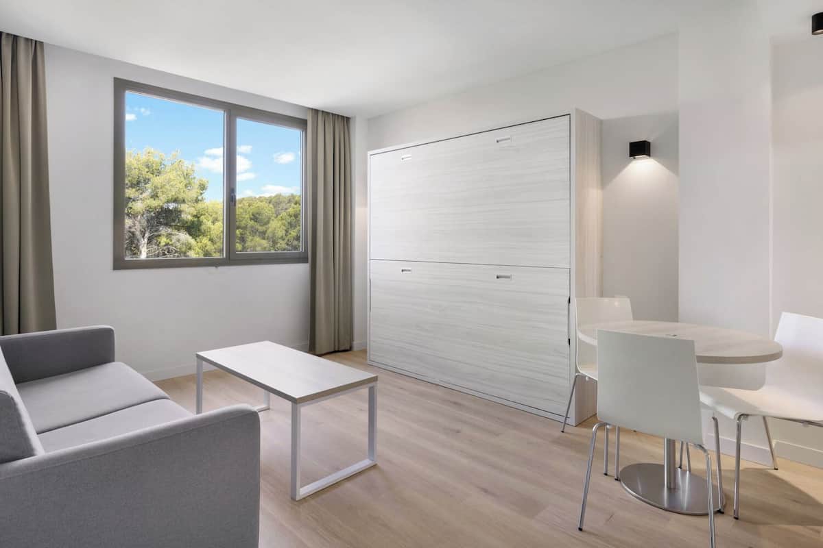 Una habitación moderna y minimalista con sofá, una mesita, un armario blanco y un comedor con mesa y sillas.
