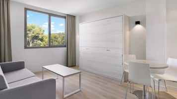 A modern, minimalist room with a sofa, a small table, a white cabinet, and a dining area with a table and chairs.