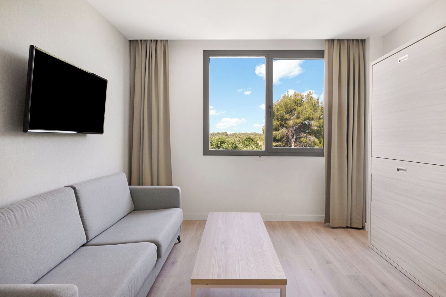 A modern room with a sofa, a table, a TV, and a window with a view of trees.