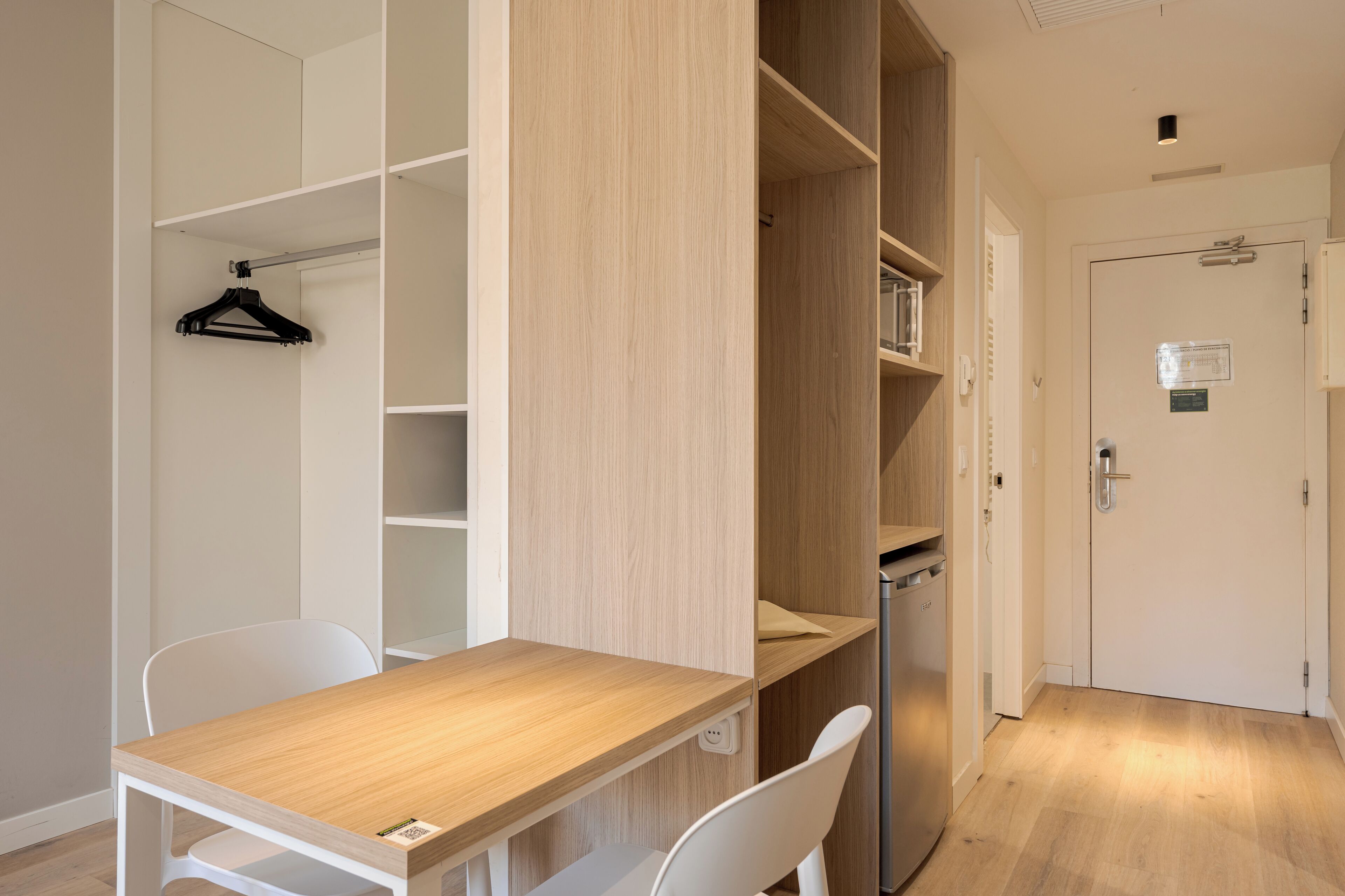 Una habitación con un escritorio de madera, sillas blancas, un perchero colgante y estanterías empotradas.