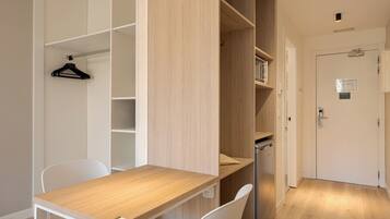 Una habitación con un escritorio de madera, sillas blancas, un perchero colgante y estanterías empotradas.