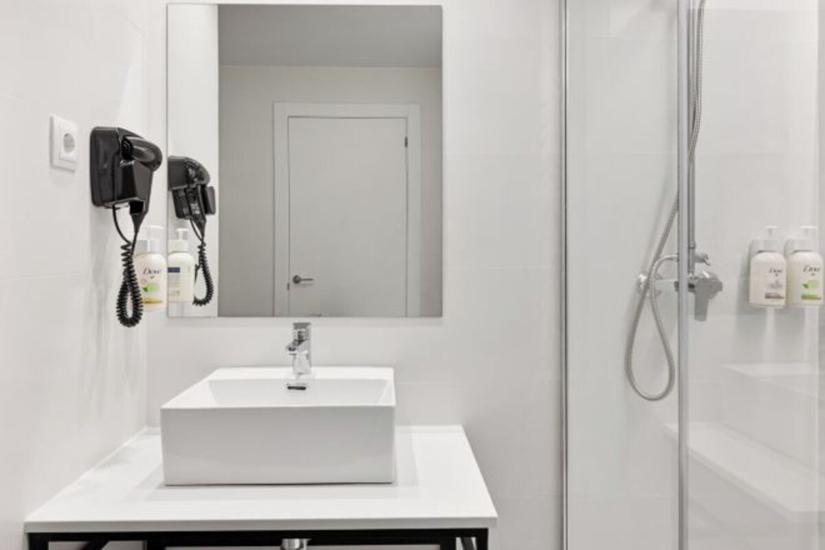 Un baño con lavamanos blanco, espejo, teléfono y ducha.