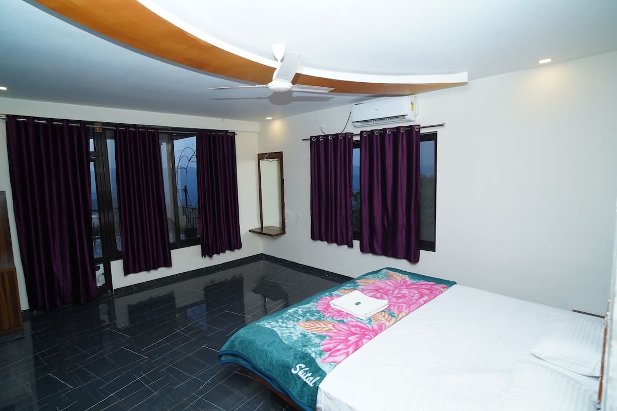 Habitación de hotel con cama, ventilador de techo, ventana grande con cortinas moradas y piso de baldosas negras.