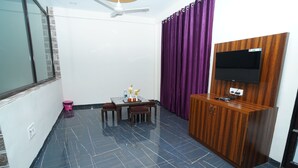 Una habitación con piso de baldosas negras, un mueble de madera con televisor de pantalla plana, una mesa de comedor con sillas y cortinas moradas.