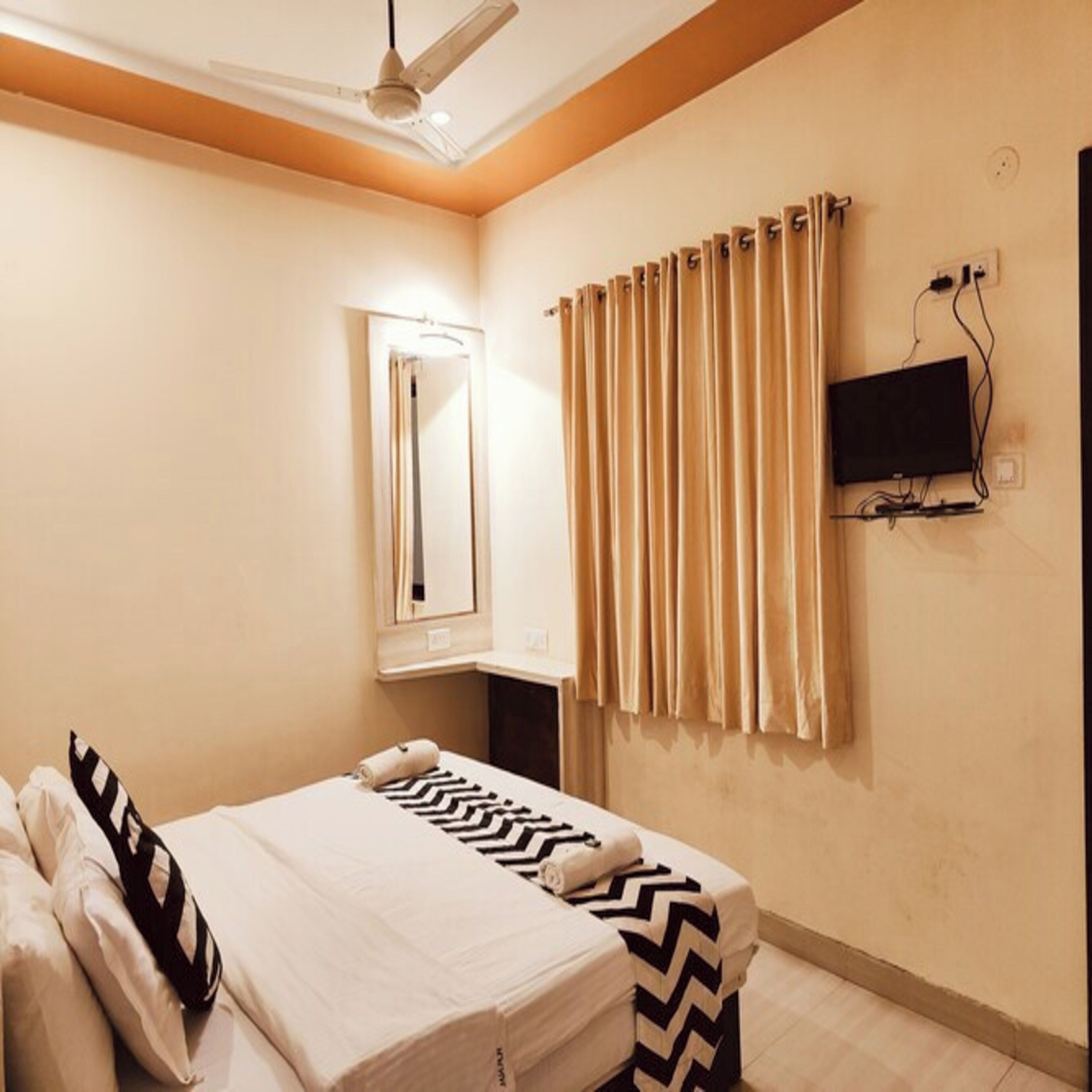 Une chambre d’hôtel avec un lit, un ventilateur de plafond, un téléviseur fixé au mur et une fenêtre avec des rideaux.