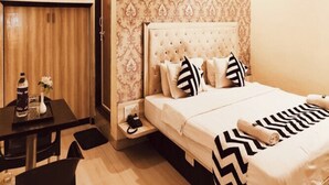 Habitación de hotel con cama, escritorio y una silla. El papel tapiz de la pared presenta un diseño y hay un ventilador de techo.