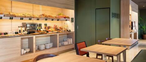 A modern cafe with wooden tables and chairs, a counter with baked goods and beverages, and a green accent wall.