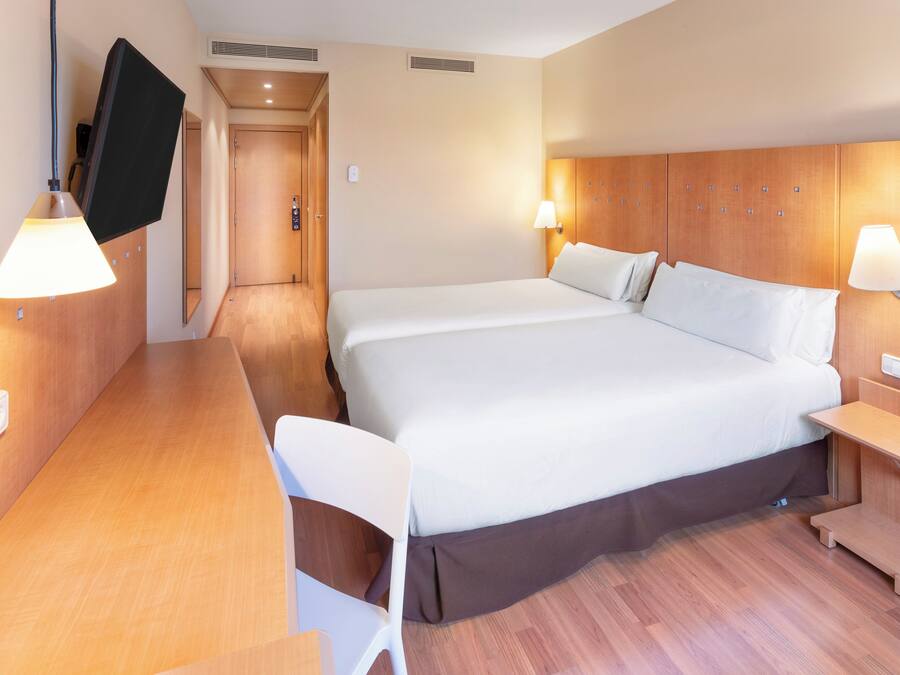 A hotel room with a large bed, bedside tables, a desk, and a TV mounted on the wall.