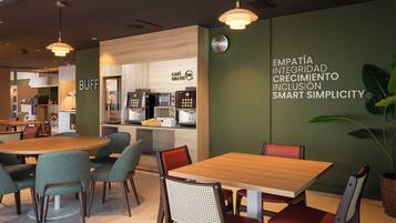 A modern cafe with wooden tables and chairs, a coffee machine, and a wall with motivational text.