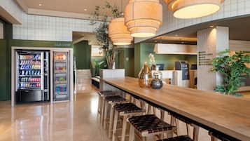 Un área de bar moderna con una barra de madera larga, varios taburetes y una máquina expendedora.