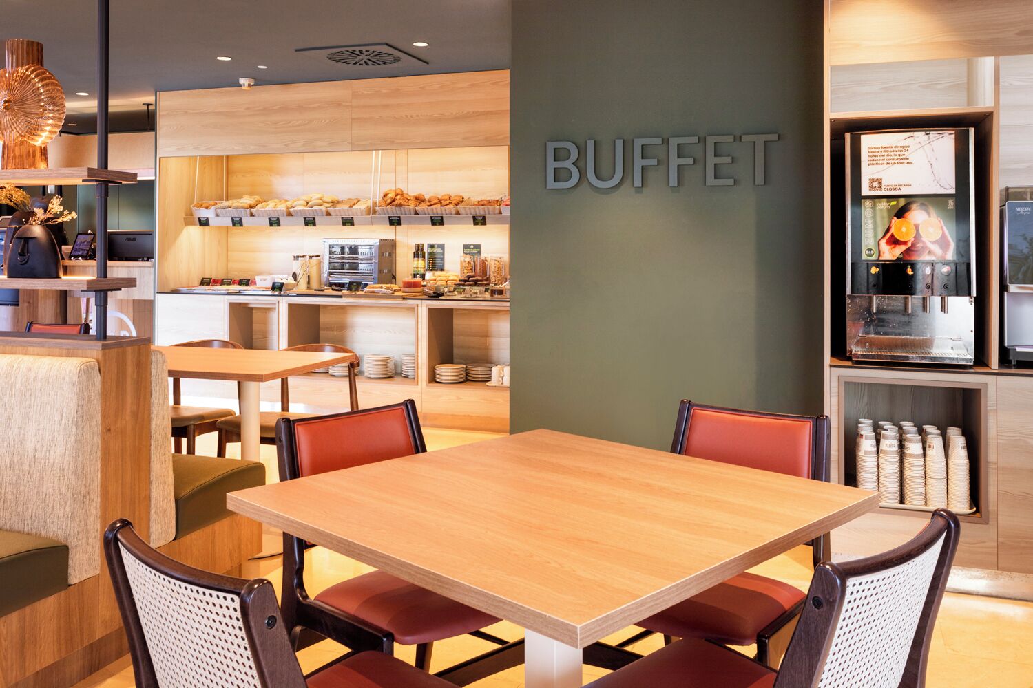 A buffet area with a wooden table and chairs, a coffee machine, and a counter with various food items.