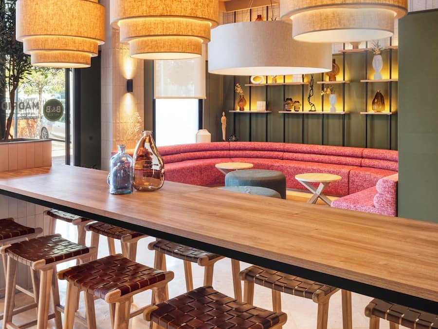 Un espace bar moderne avec un long comptoir en bois, de nombreux tabourets et des lampes suspendues.