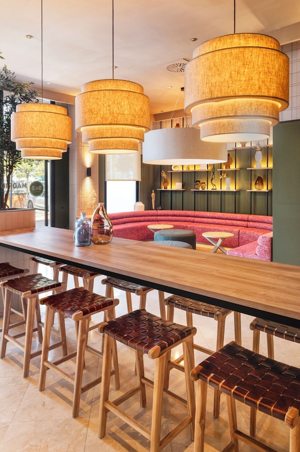 Un espace bar moderne avec un long comptoir en bois, de nombreux tabourets et des lampes suspendues.