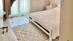 A bedroom with a bed, a chandelier, a window with curtains, and a bedside table. - Marble Luxury Villa in Neapolis (Αγιος Νικολαος)