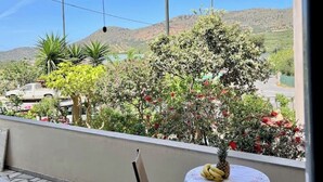 A balcony with a table and chairs, overlooking a garden with various plants and a mountain in the background. - Marble Luxury Villa in Neapolis (Αγιος Νικολαος)
