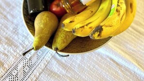 A bowl containing a pineapple, bananas, a pear, a bottle of olive oil, and a bottle of wine on a table with a white tablecloth. - Marble Luxury Villa in Neapolis (Αγιος Νικολαος)