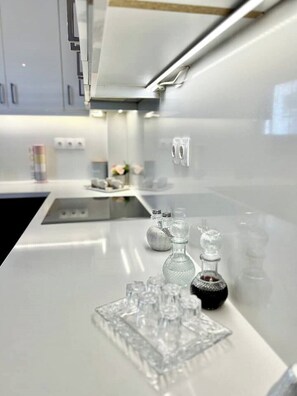 A modern kitchen with a white countertop, stainless steel appliances, and a glass display case with bottles and glasses.