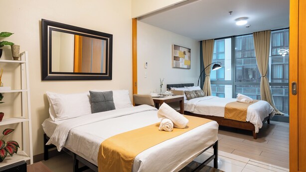 Ett hotellrum med två sängar, ett matbord, en spegel och utsikt över staden genom stora fönster.