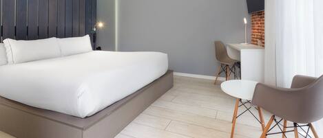 A modern bedroom with a large bed, a desk, two chairs, and a TV mounted on a brick wall.