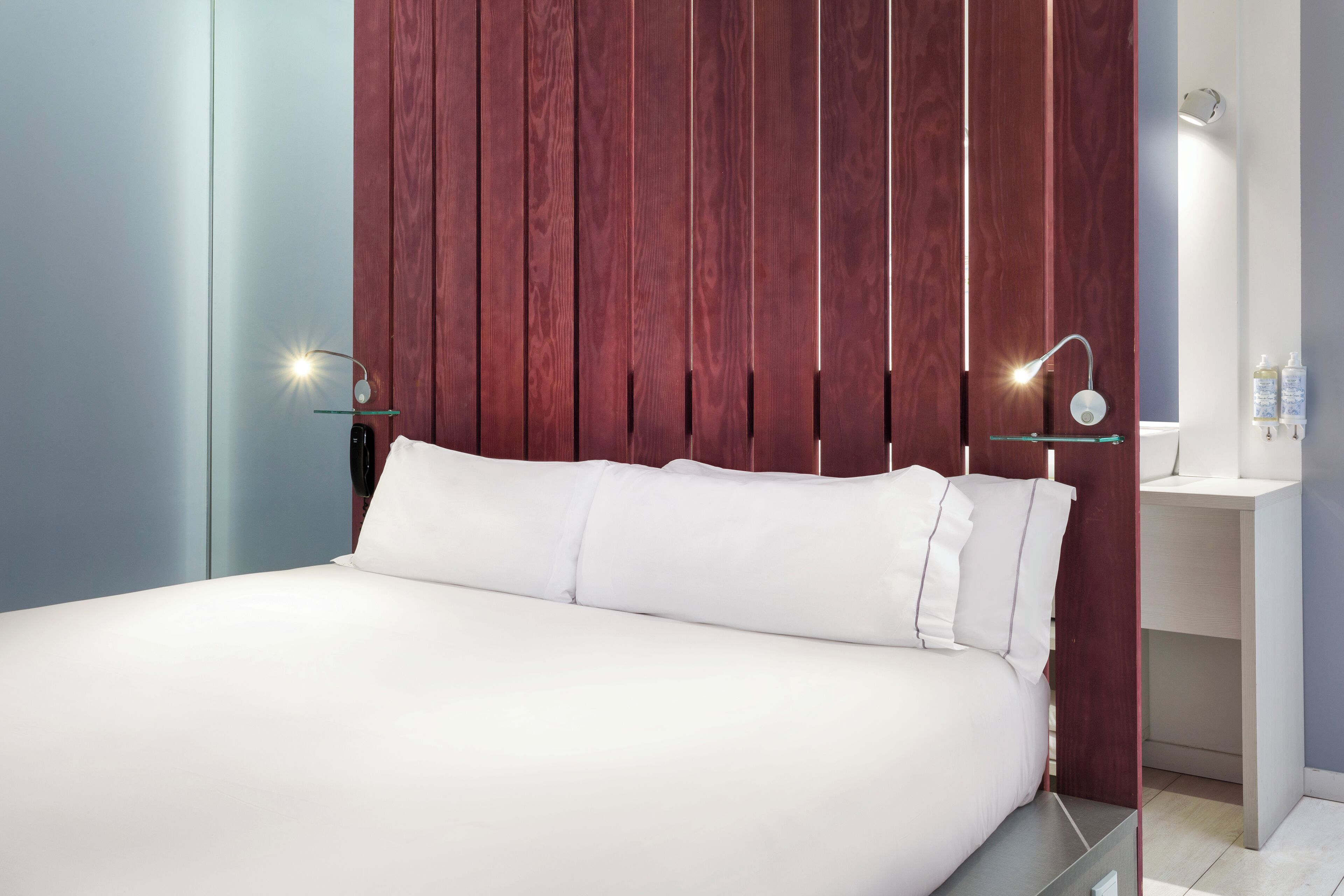 Une chambre moderne avec un grand lit, un mur lambrissé en bois, des tables de chevet et des luminaires fixés au mur.