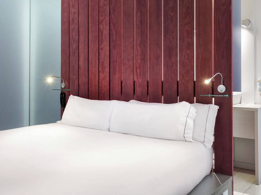 Un dormitorio moderno con una cama grande, panel de pared de madera, mesitas de noche e iluminación empotrada.