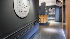 Un hall d’accueil d’hôtel avec un panneau circulaire portant l’inscription « B&B HOTELS » et un comptoir de réception.