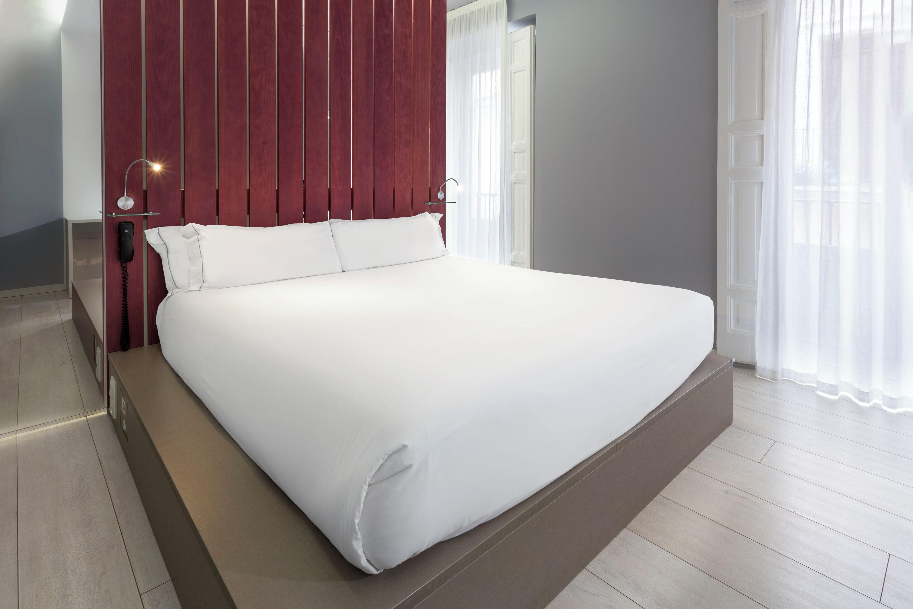 Camera d'albergo moderna con un letto grande, testiera in legno e telefono sul comodino.