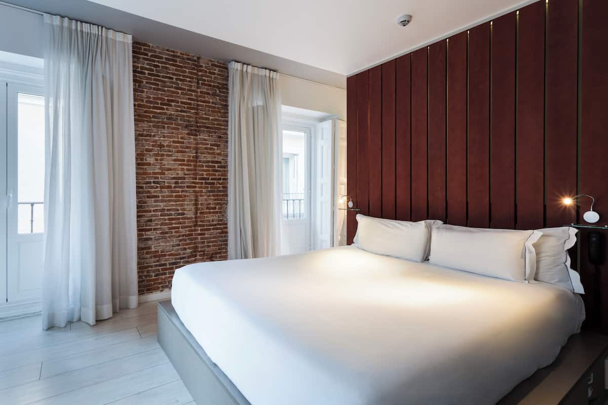 A modern bedroom with a large bed, a brick wall, and a wooden panel wall.