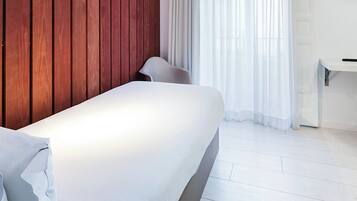 A modern bedroom with a wooden headboard, a white bed, a white bedside table, and a chair.