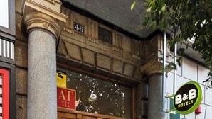 L’entrée d’un hôtel, avec une grande porte en bois, des colonnes en pierre et une enseigne indiquant « B&B Hotels ».