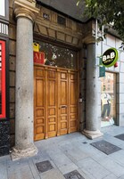 L’entrée d’un hôtel, avec une grande porte en bois, des colonnes en pierre et une enseigne indiquant « B&B Hotels ».