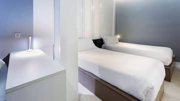 A modern hotel room with two single beds, a bedside table, a nightstand, and a large window with blinds.