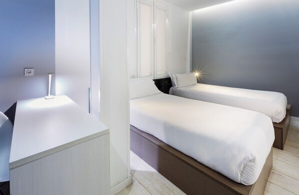 A modern hotel room with two single beds, a bedside table, a nightstand, and a large window with blinds. - B&B Hotel Madrid Centro F52 (Madrid)