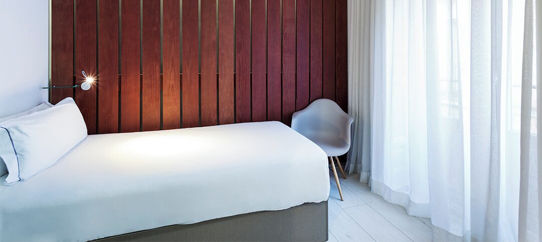 A modern bedroom with a bed, a chair, and a wooden wall panel.
